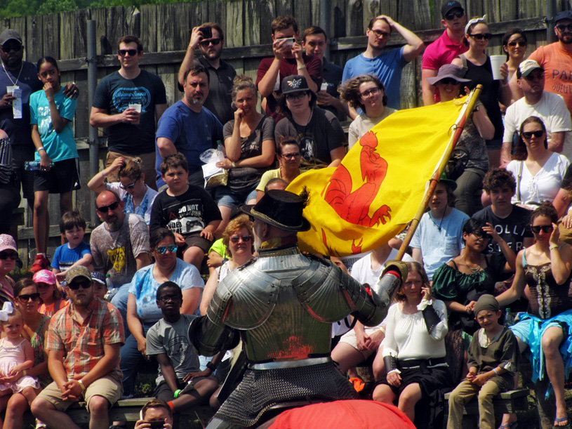 View from backside of monyed knight facing a large crowd, He banner is blowing in thw wind.