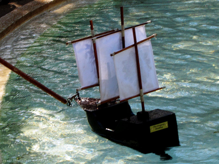 Man in burgandy renaissance coat. He is holding a handmade wooden boat.
