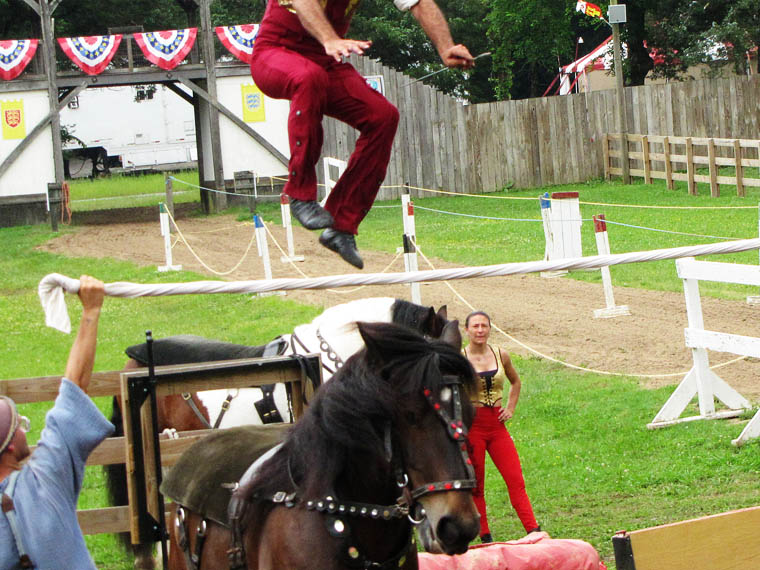 Man jumping in air. he's jumping over a rope two men sevral feet are holding over their heads. The jumping man was riding a horse, jumped over the ropand laned safely on the horse. 