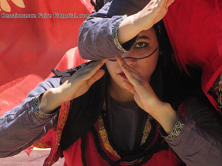 woman making a triangle with her hands. her face is covered by another woman's arm in same position, you can only see one eye peering as most her face is covered by the other woman's arm.