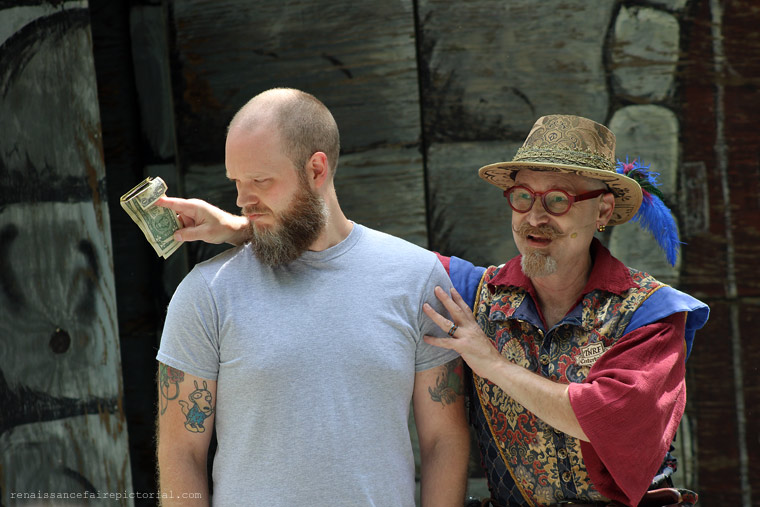 two men on stage . one has his arm behind the other. he showing the other man money that he pull of the other's wallet.